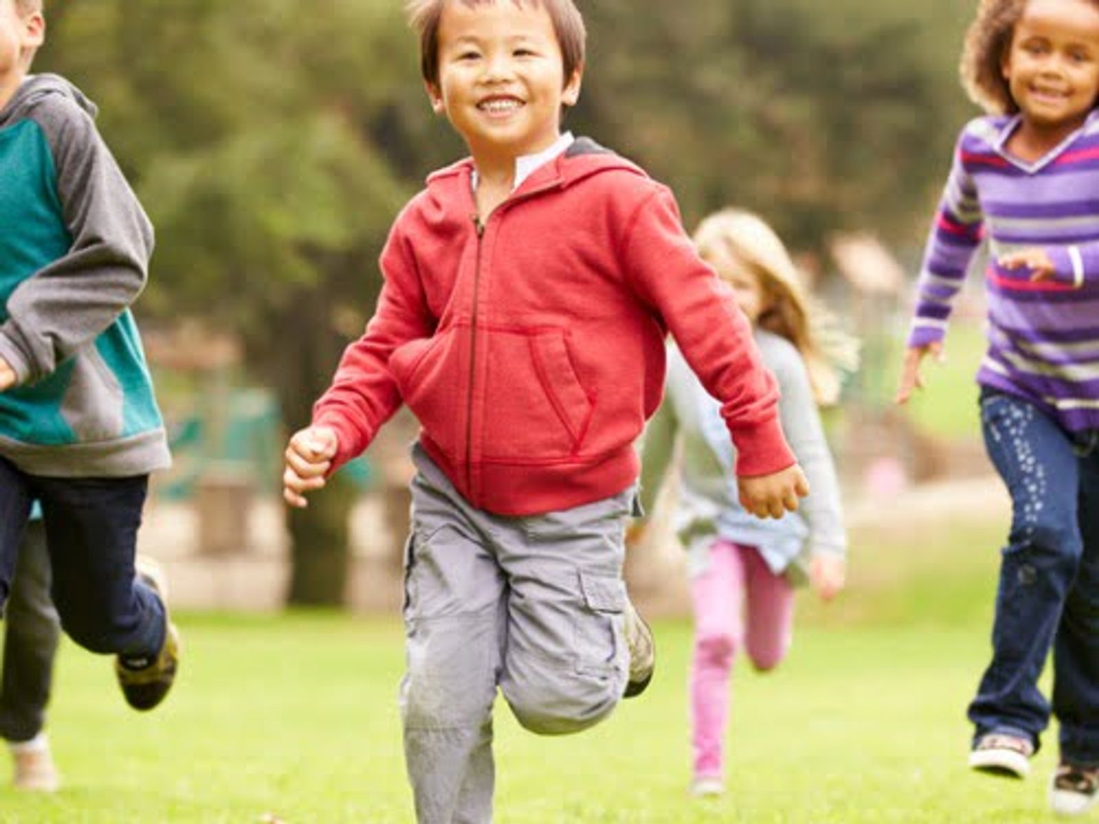 Group of children running together on grass outdoors in a park setting.