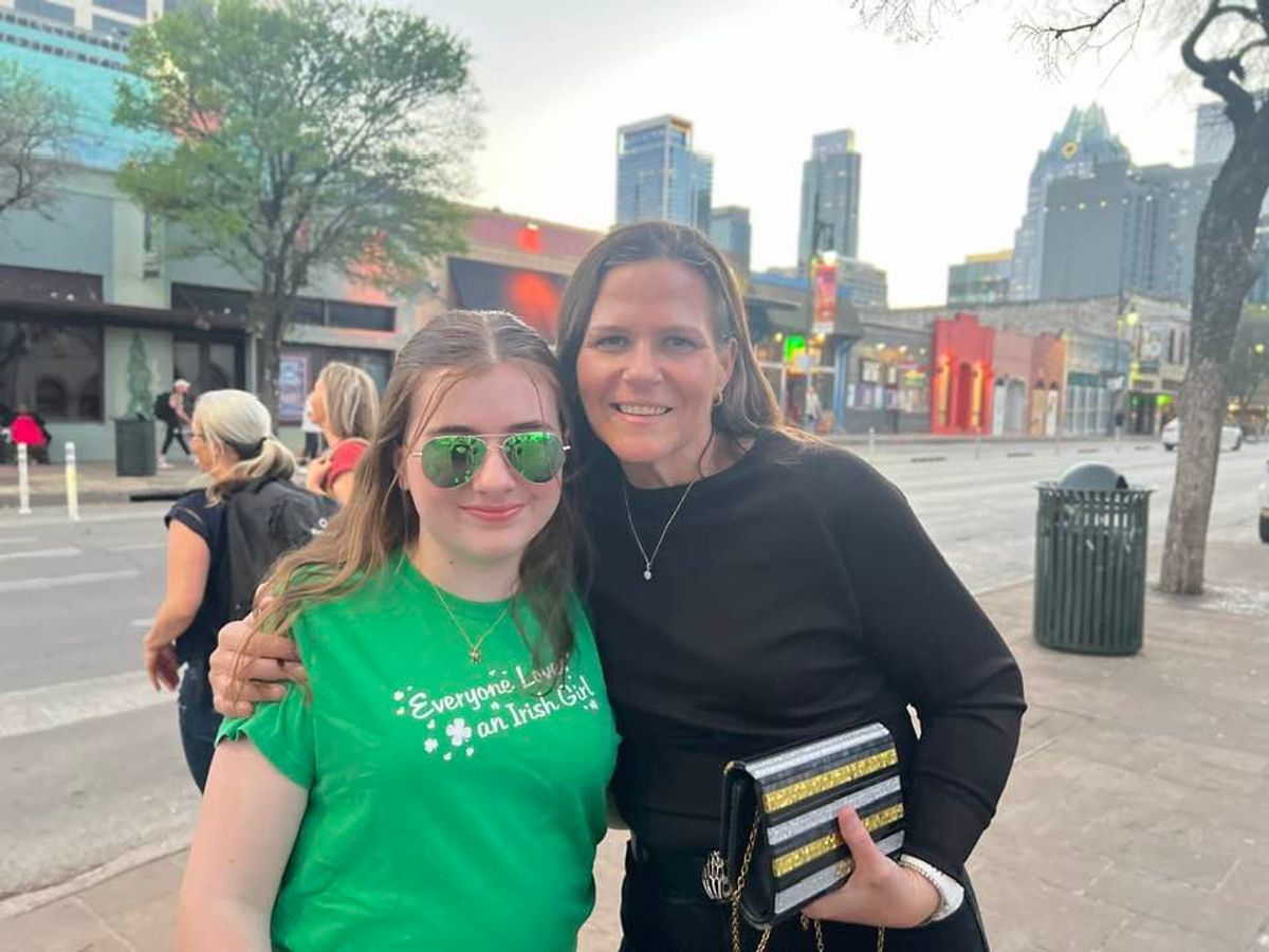 Two women smiling at camera in urban plaza with city skyline background.