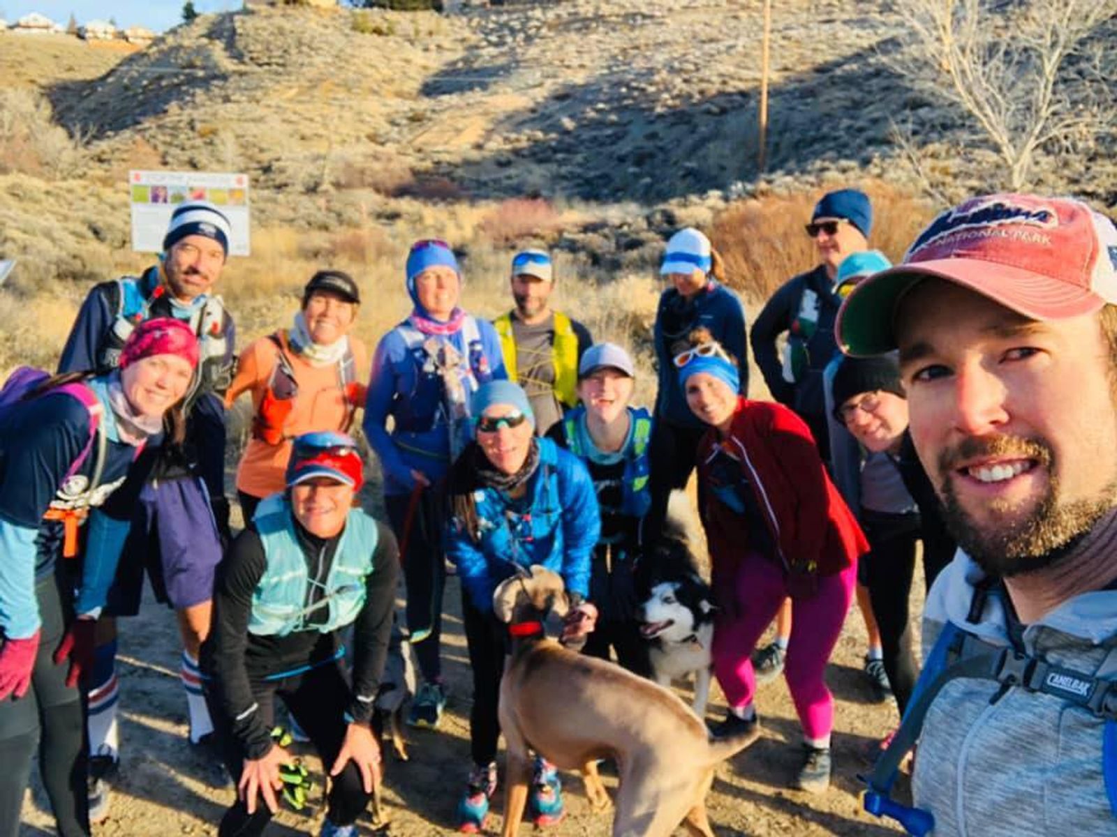 Large group of people wearing blue caps and athletic gear posing outdoors on hillside with dog.
