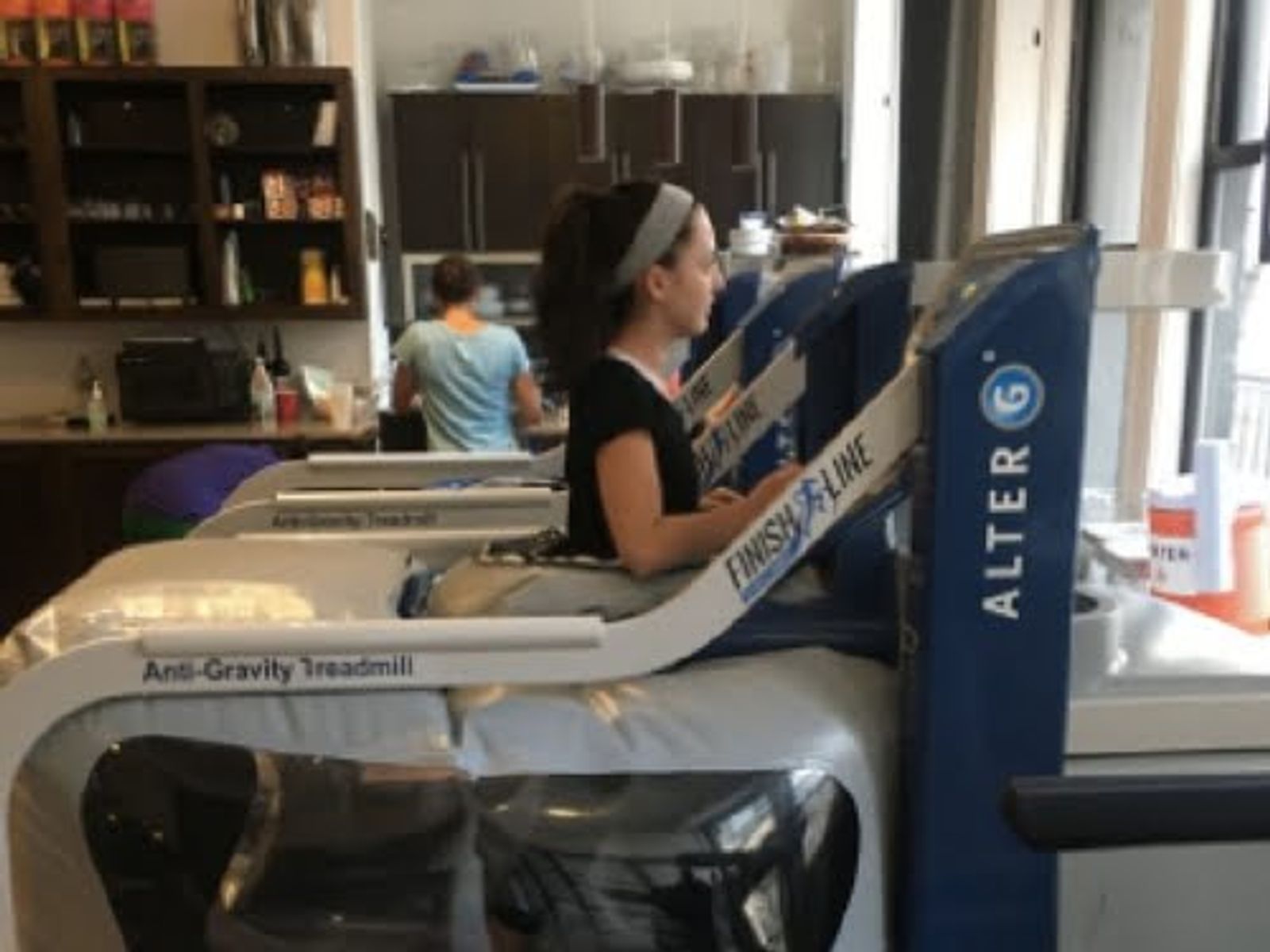 Woman using Anti-Gravity Treadmill in fitness studio with exercise equipment visible.