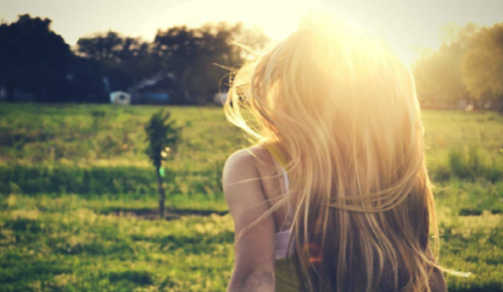 Woman with long blonde hair viewing sunny rural field and distant farmhouse.