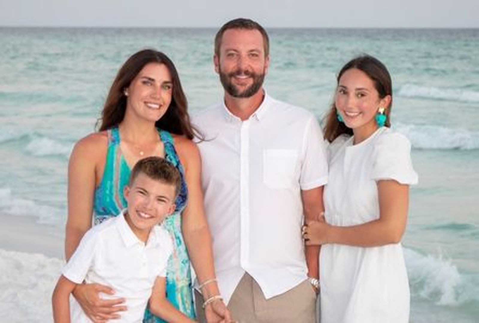 Familia de cuatro personas sonriendo en una playa con olas del océano de fondo.