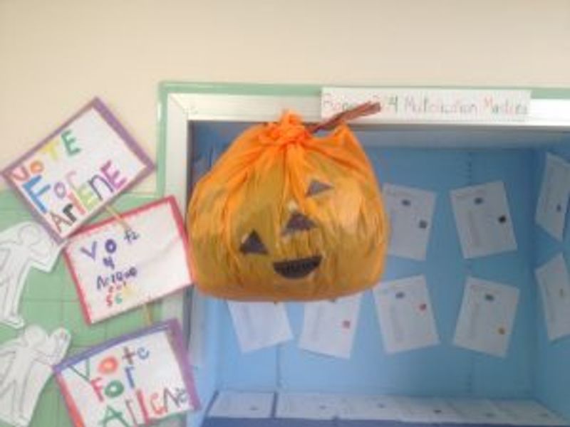 Handmade jack-o'-lantern pumpkin decoration hanging in classroom display box with student work.