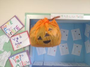 Decoración artesanal de calabaza jack-o'-lantern colgada en una caja de exhibición del salón de clases con trabajos de estudiantes.
