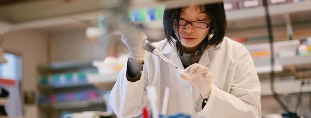 Female scientist in white lab coat and glasses conducting experiment in laboratory setting.