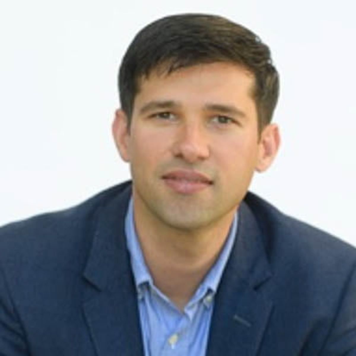 Professional headshot of a man in dark blazer and light blue shirt against white background.