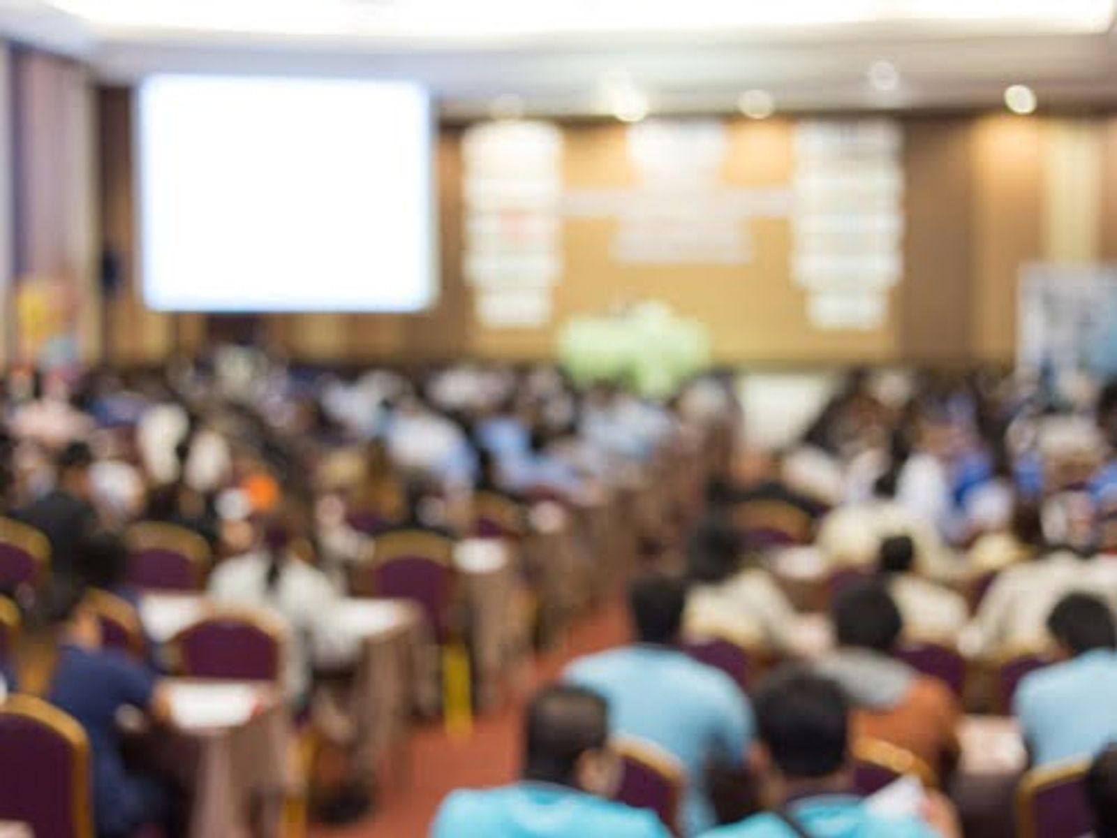 Blurred view of large conference hall with seated audience and projection screen.