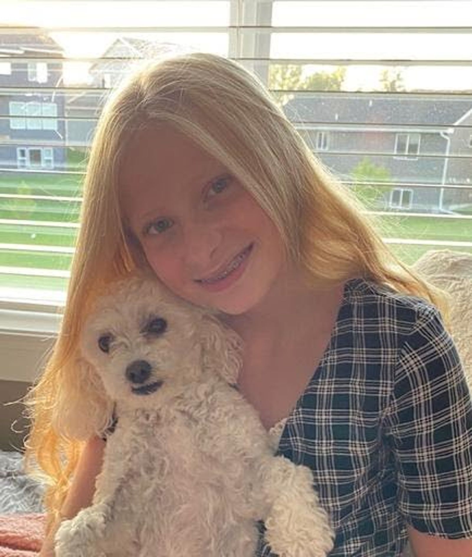 Woman with long reddish-blonde hair holding small tan curly-haired dog, smiling at camera indoors.