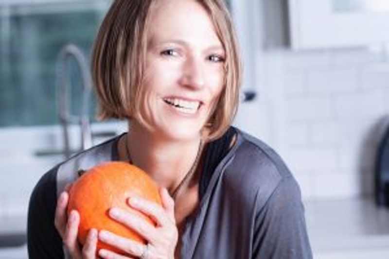 Woman holding orange grapefruit, smiling in modern kitchen setting.