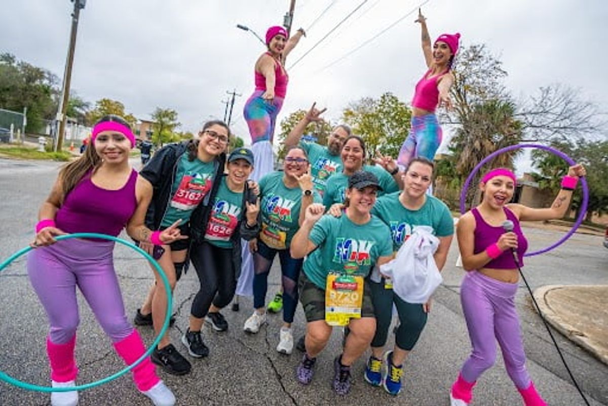 Group of people in bright pink and purple workout attire with hula hoops on residential street.