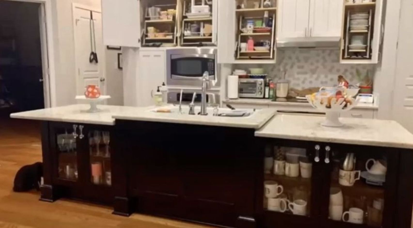 Modern kitchen with dark island, white countertops, and light cabinetry with glass doors.