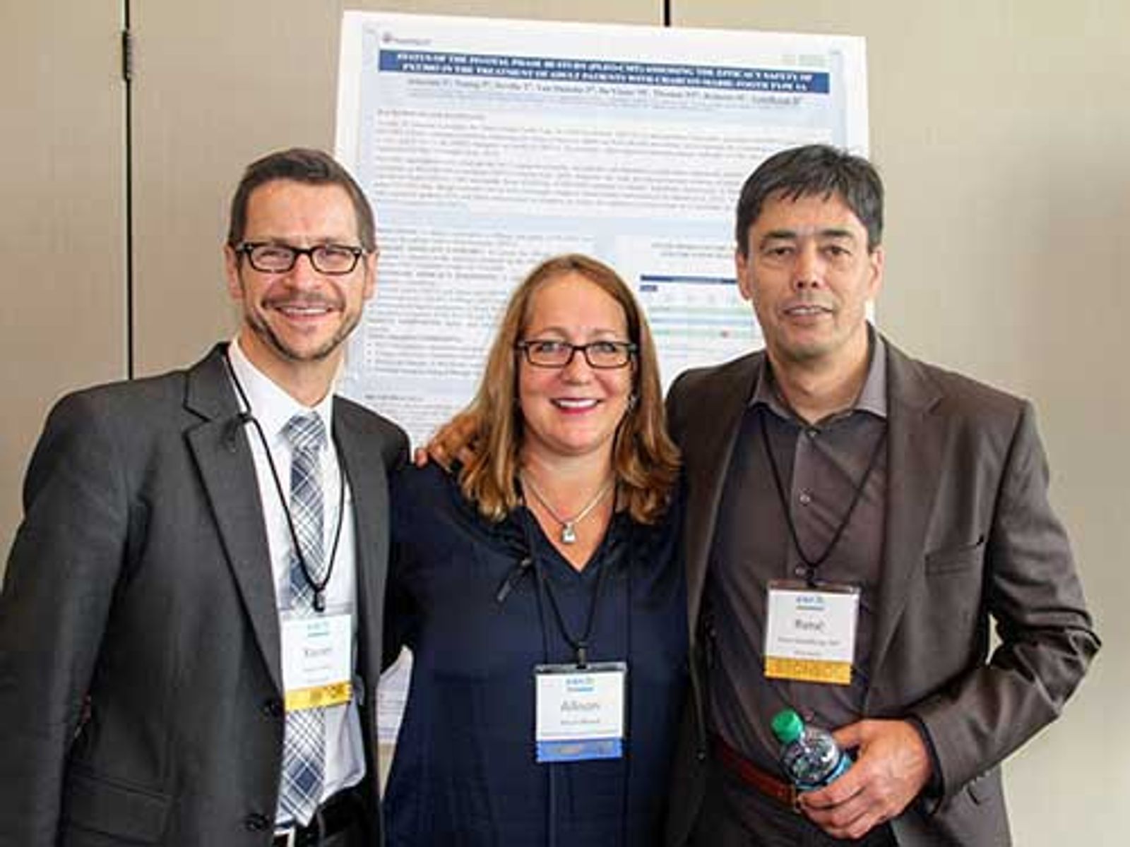 Three professionals wearing conference badges stand together in front of a research poster presentation.