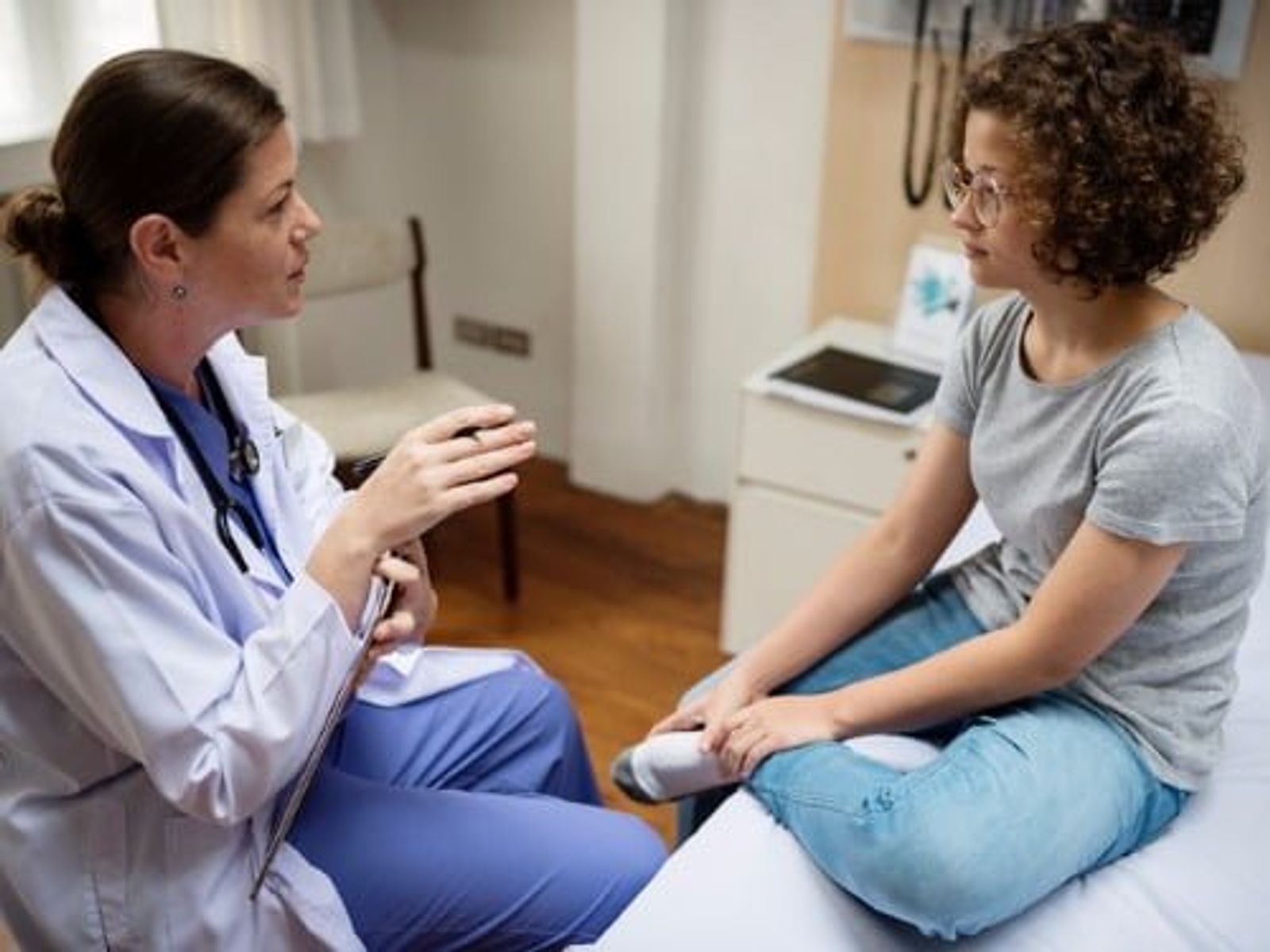 Healthcare provider in white coat consulting with patient in clinical examination room.