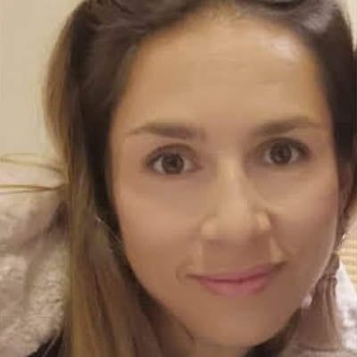 Retrato de cerca de una mujer con cabello castaño y lápiz labial rosa, que sonríe a la cámara en interiores.
