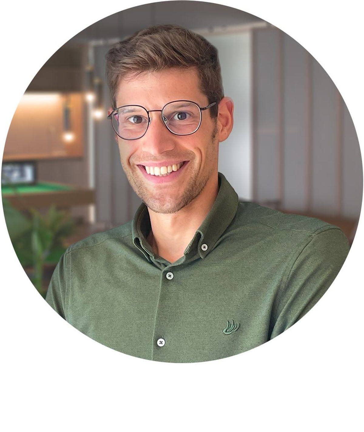 Man wearing glasses and green button-up shirt, smiling at camera in indoor setting.