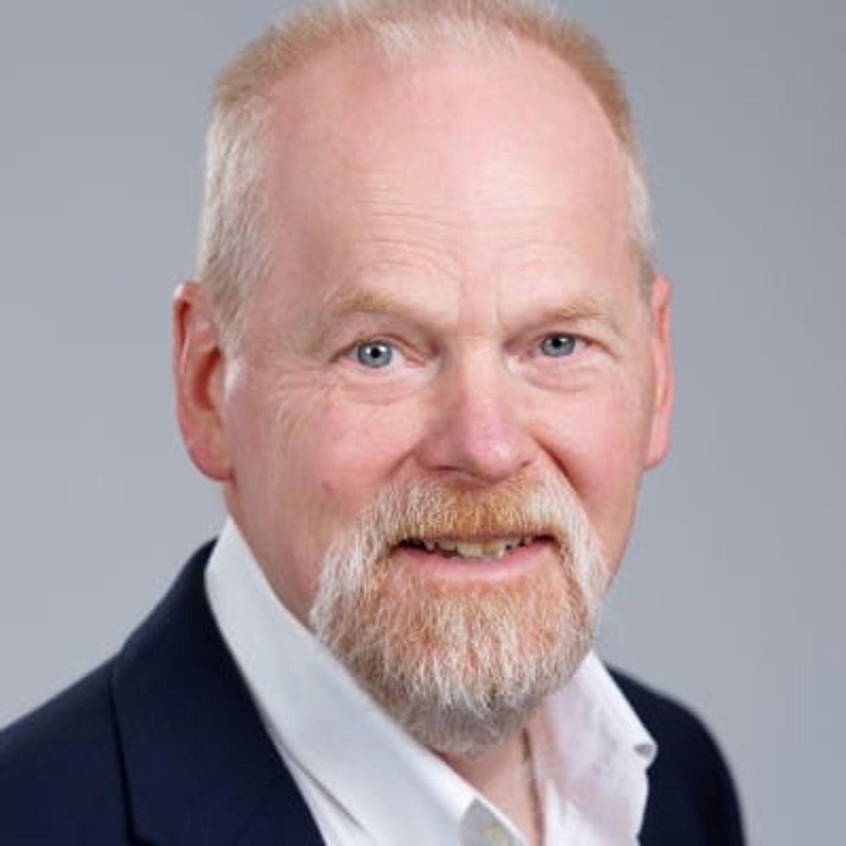 Professional headshot of an older man with gray hair and beard wearing a dark blazer and white shirt.