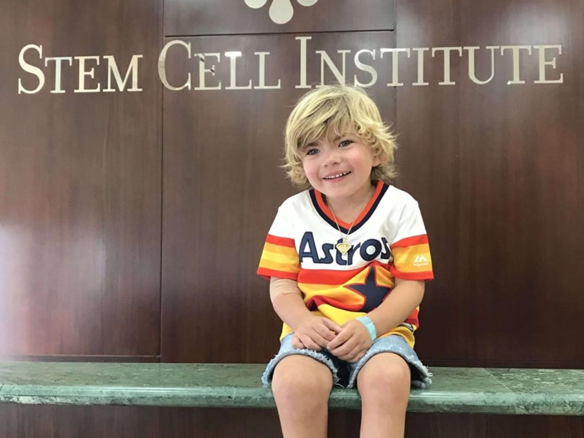 Niño pequeño con camiseta de béisbol de los Astros sentado frente a un letrero del Stem Cell Institute