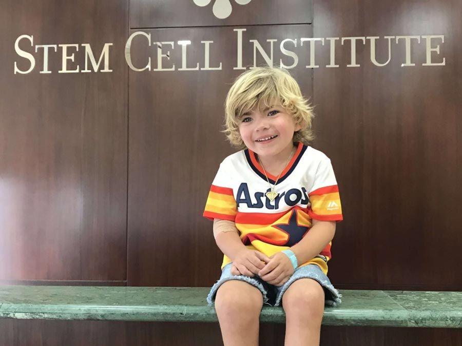 Young child in Astros baseball jersey sitting in front of Stem Cell Institute sign