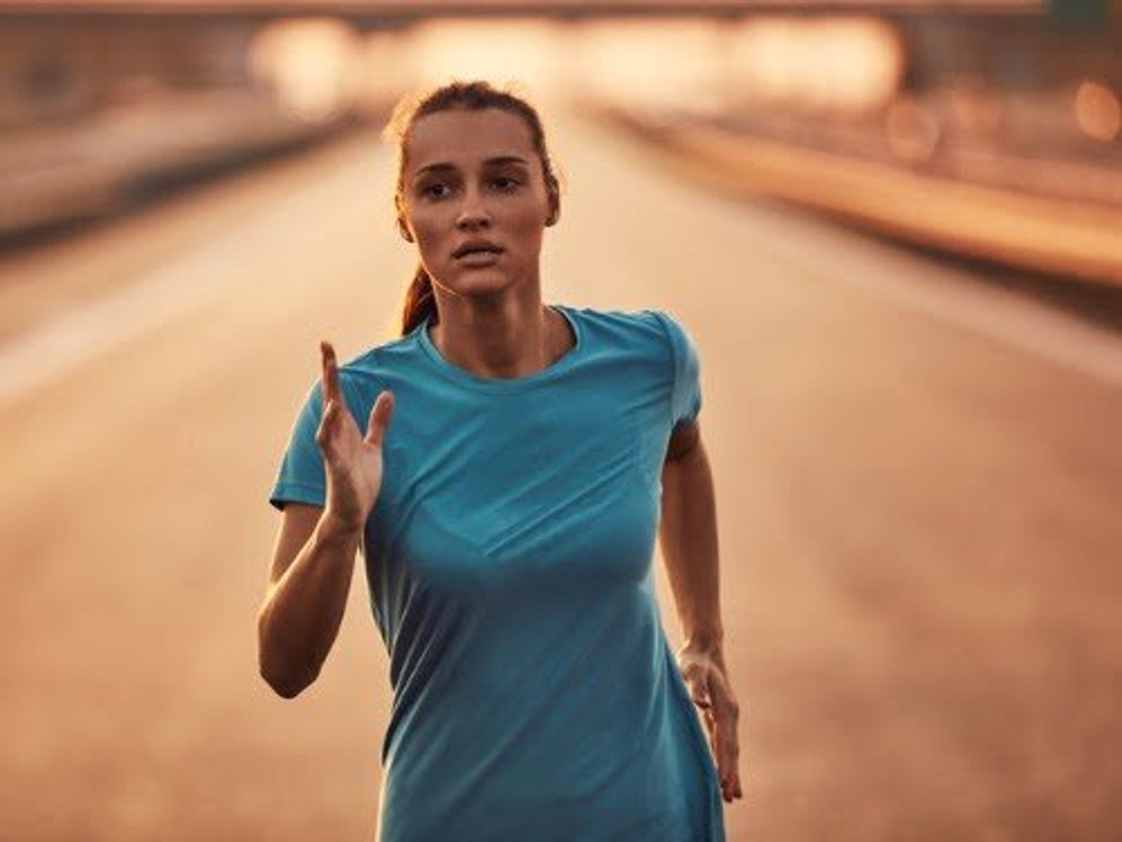 Woman in blue t-shirt running on empty desert road at sunset.