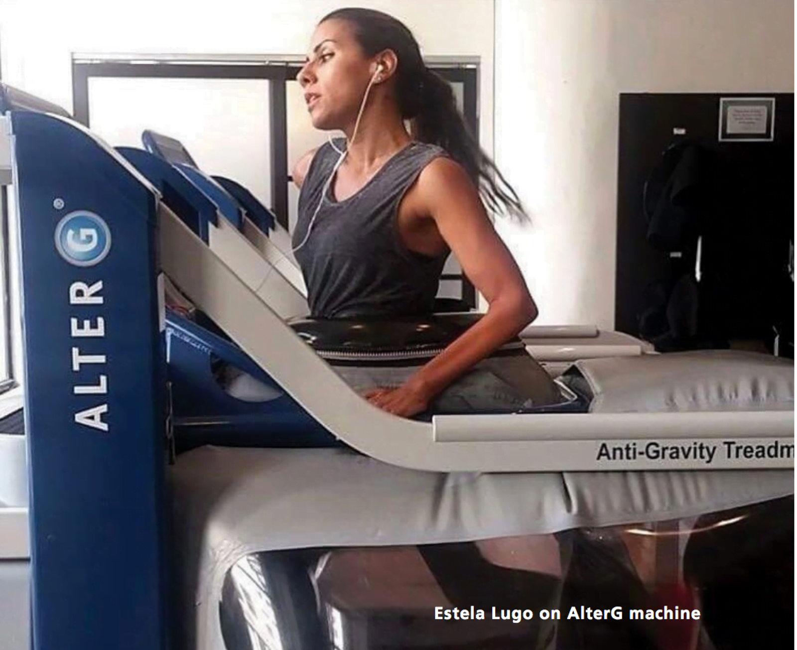 Mujer usando una caminadora antigravedad AlterG en un gimnasio interior con audífonos.