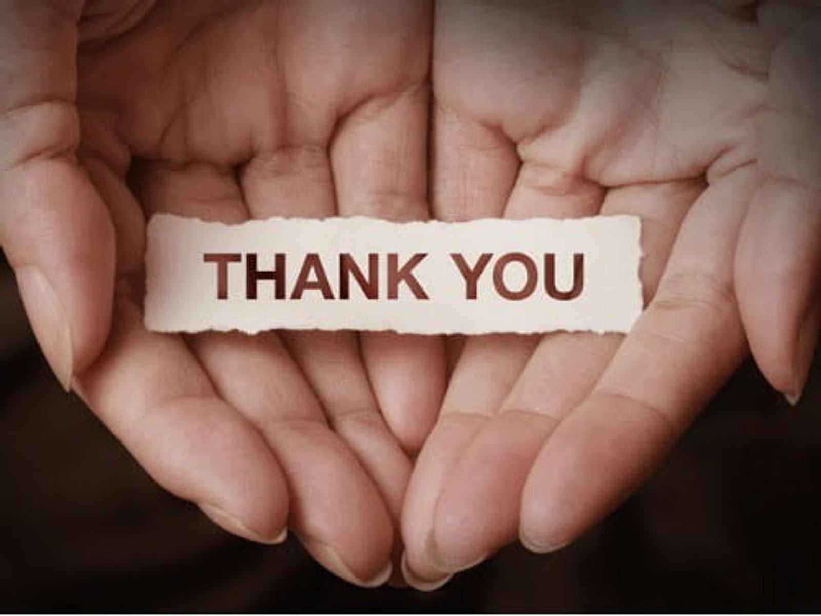 Cupped hands holding a white paper strip reading "THANK YOU" against dark background