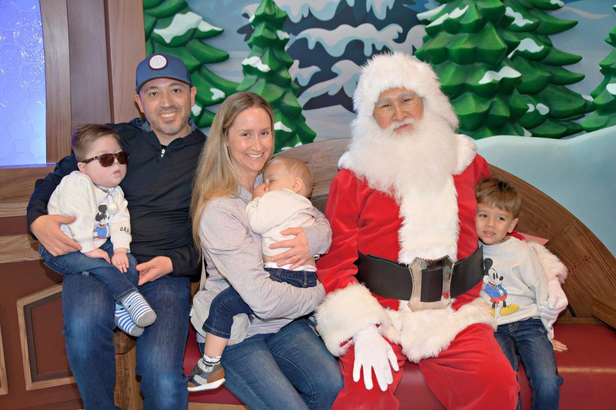 Family of five posing with Santa Claus in front of winter-themed backdrop.