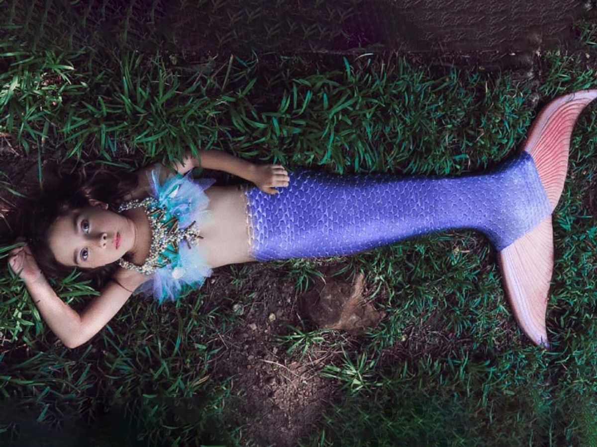 Child in mermaid tail costume lying on grass, top-down view.
