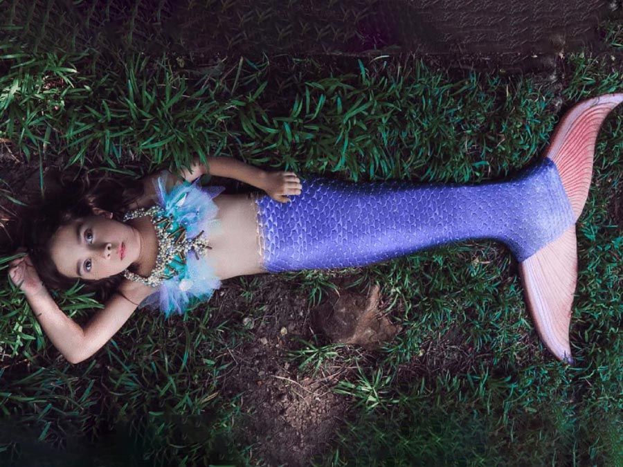 Niña con disfraz de cola de sirena acostada sobre el césped, vista desde arriba.