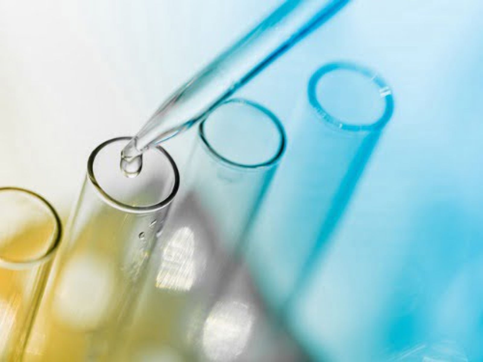 Laboratory test tubes with colored liquids and dropper pipette on blue background.
