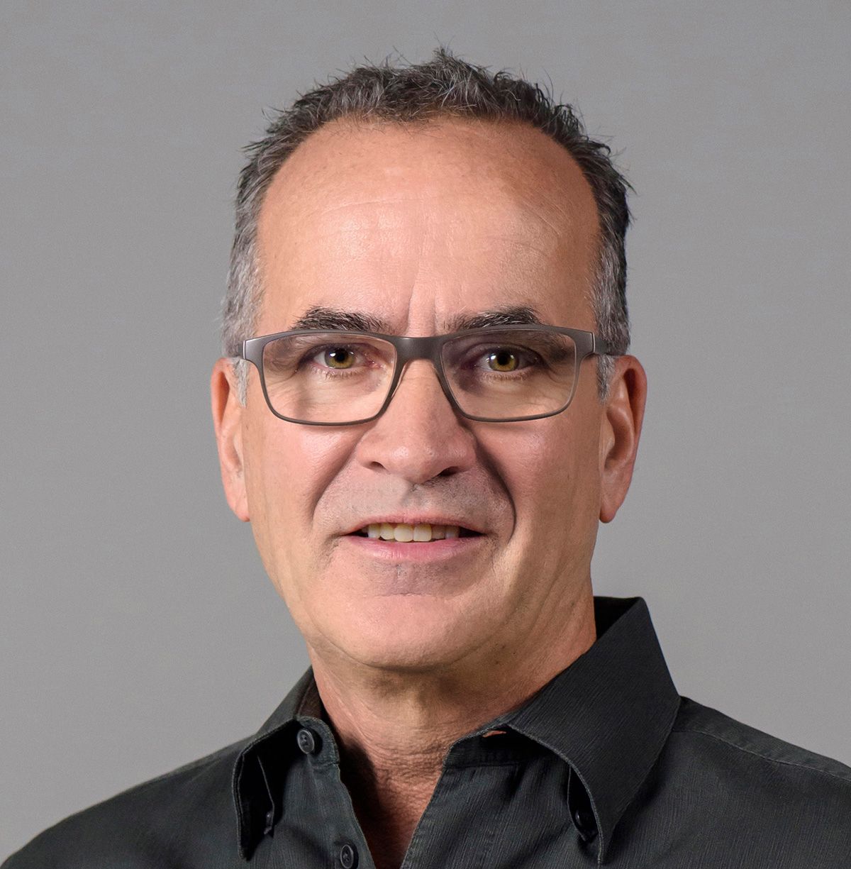 Middle-aged man with glasses wearing a black shirt against gray background