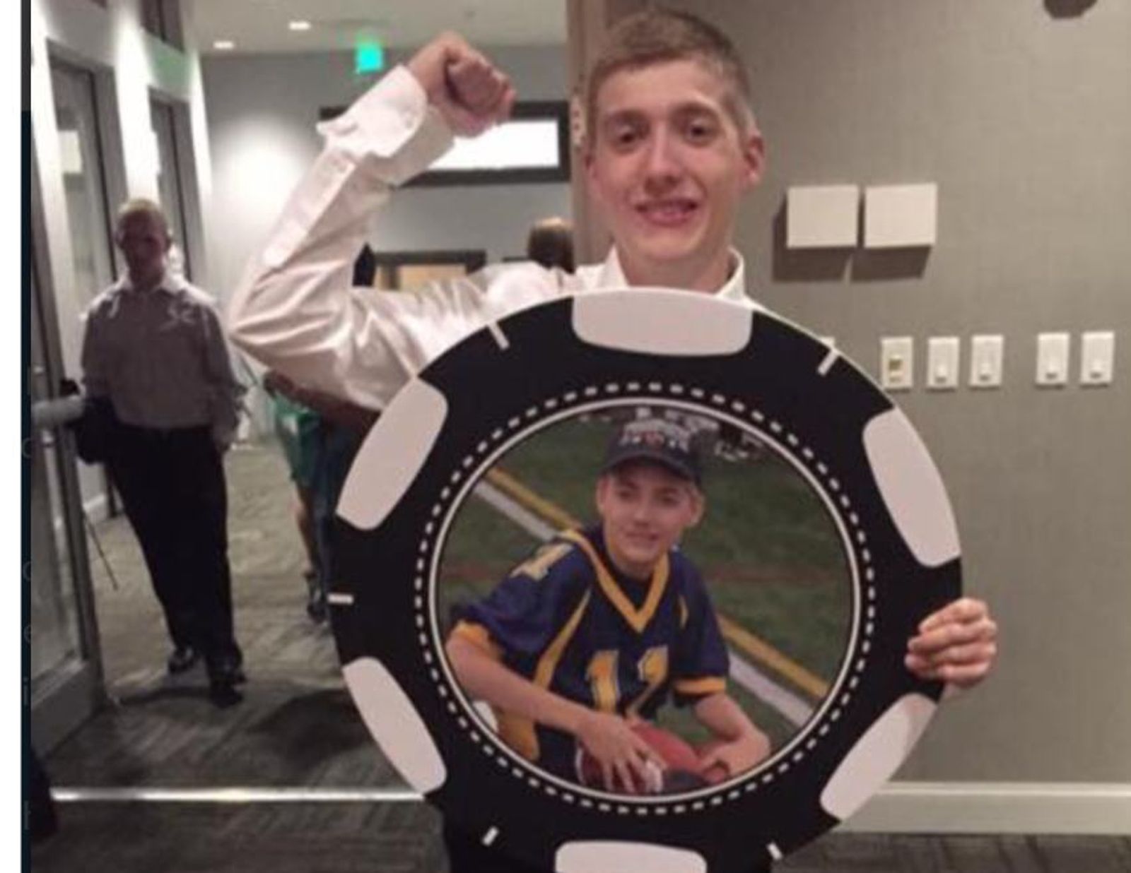 Hombre sostiene en interiores un marco circular que muestra la foto de un joven jugador de béisbol.