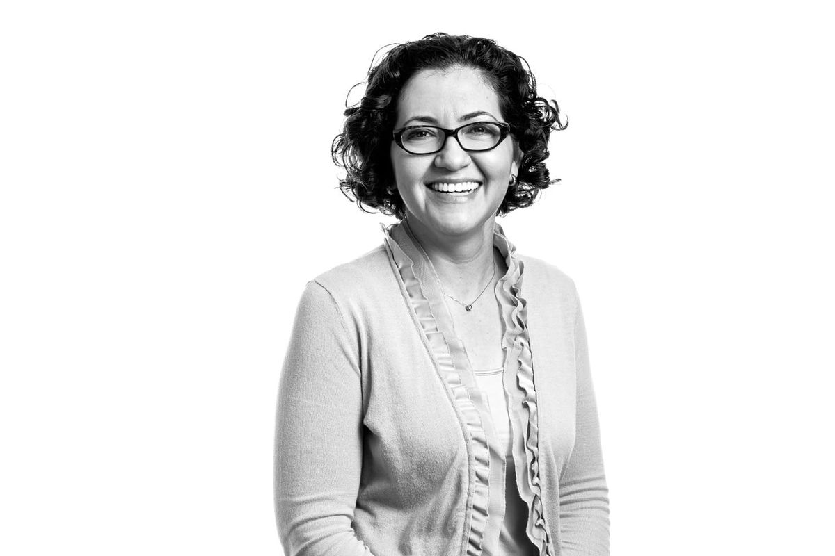 Black and white portrait of a smiling woman wearing glasses and a cardigan with a scarf.
