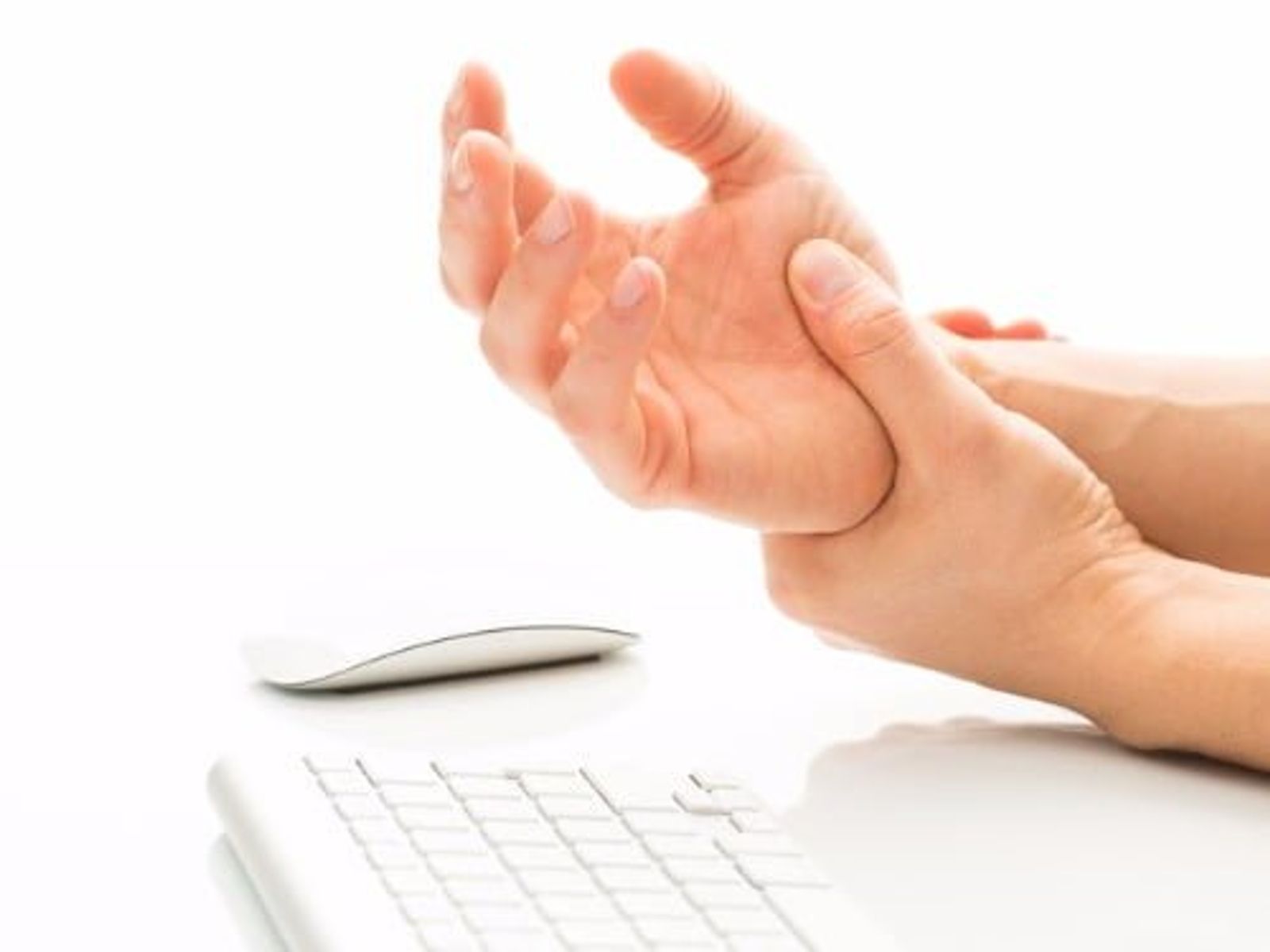 Person holding wrist in pain near computer keyboard and mouse.
