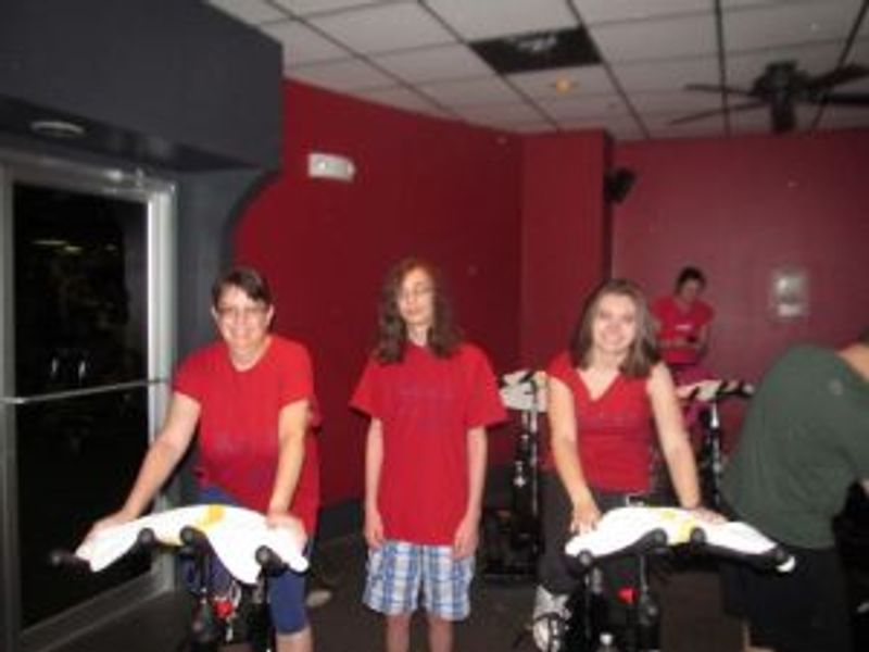 Three girls in red shirts holding white clothing in red-walled indoor space.