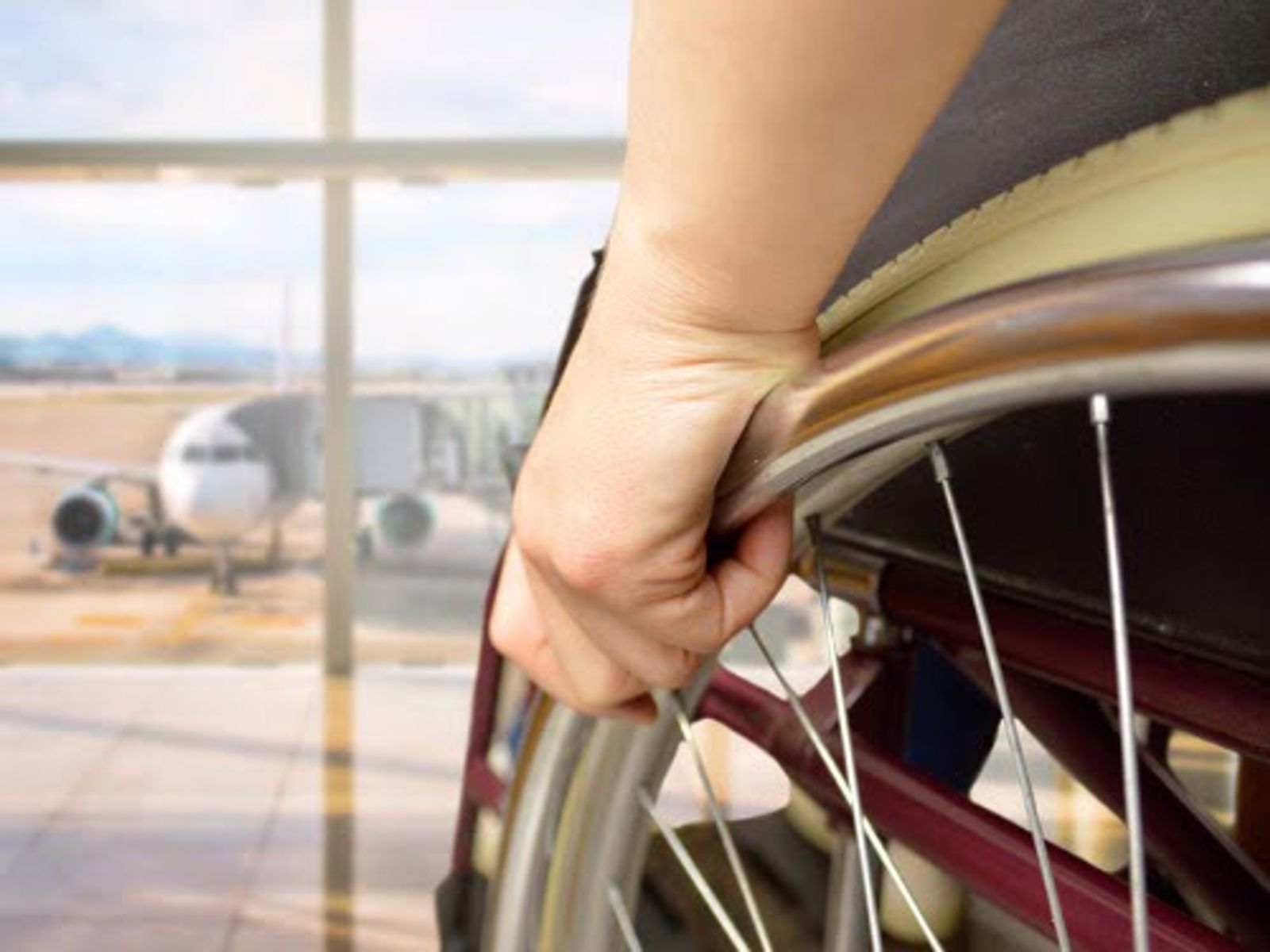 Hand gripping airport window railing with airplane visible on tarmac outside.