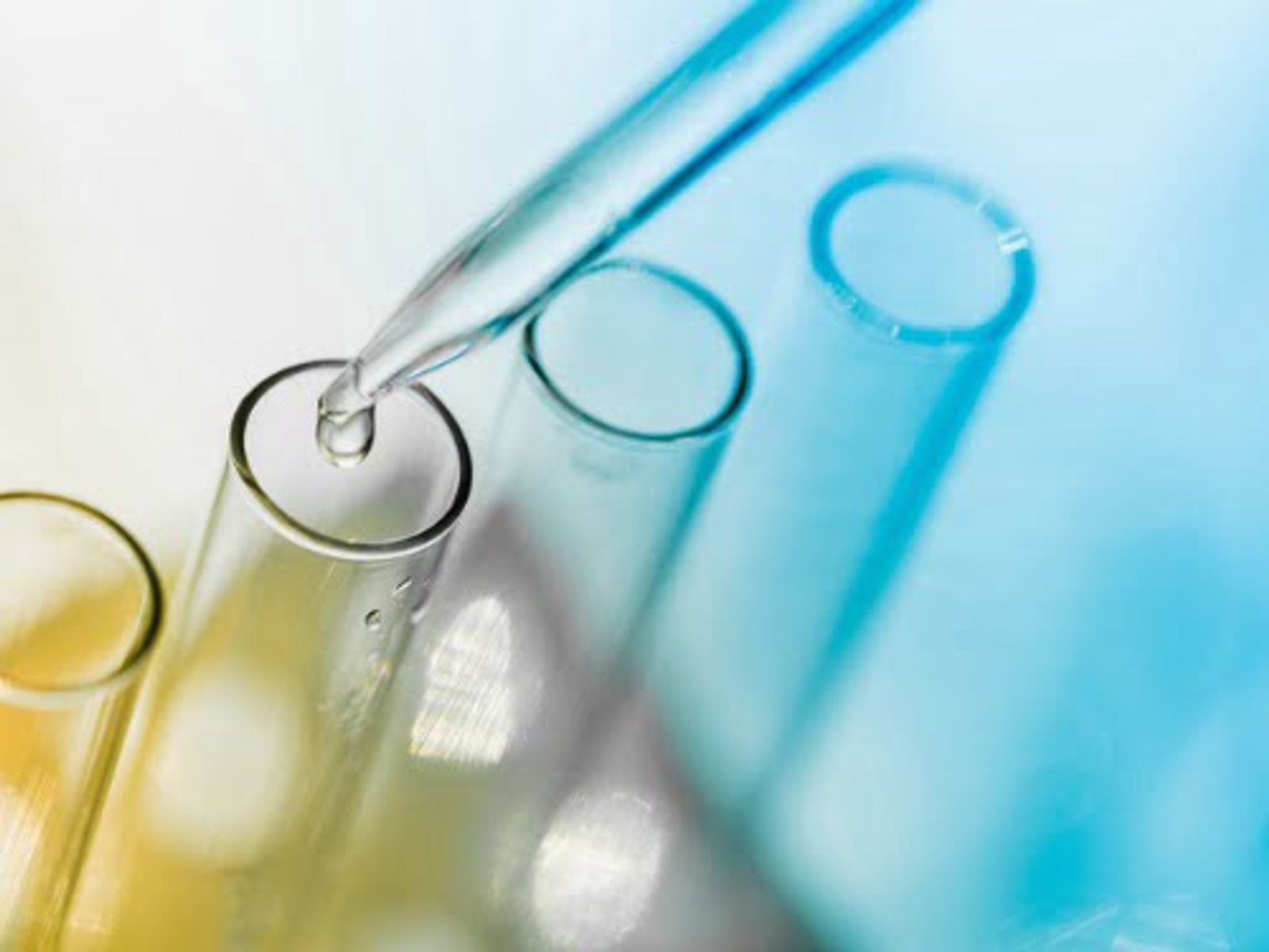 Laboratory test tubes with yellow and blue liquids and a pipette on blue background.