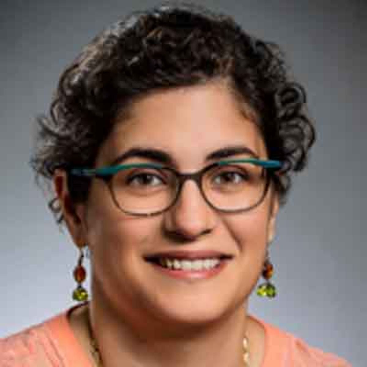 Portrait of a person wearing glasses and an orange shirt, smiling at the camera.