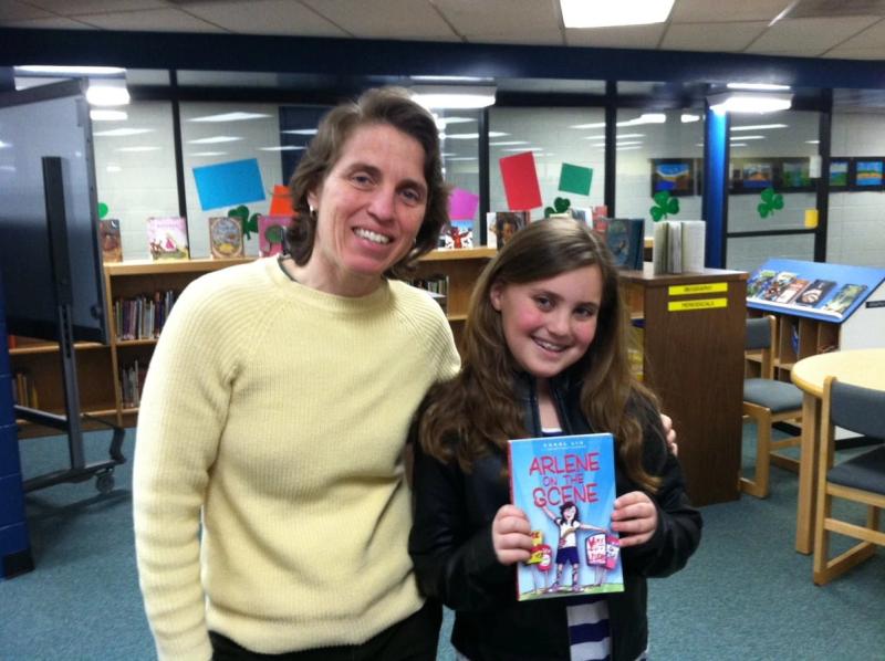 Two smiling people in a library holding an "Arlene Sardine" book.