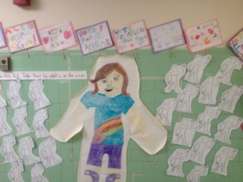 Classroom bulletin board display with colorful paper figure and student artwork samples.