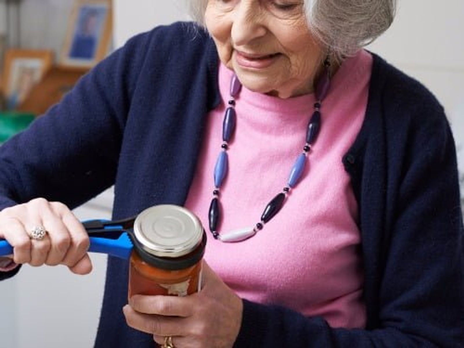 Elderly woman using a jar opener to open a glass jar with metal lid.