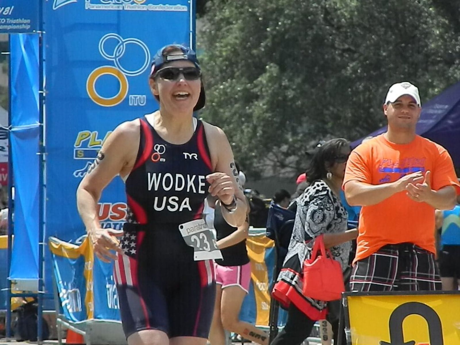 Triathlon competitor wearing "WODKE USA" race bib running past spectators at outdoor event.