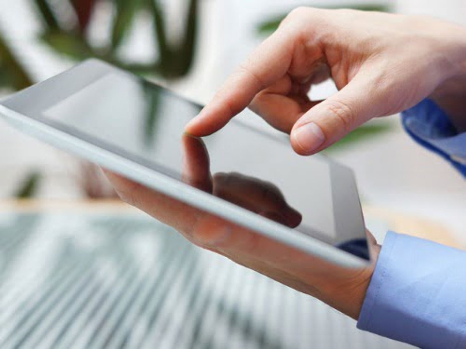 Person's hand touching tablet screen outdoors with blurred green foliage background.