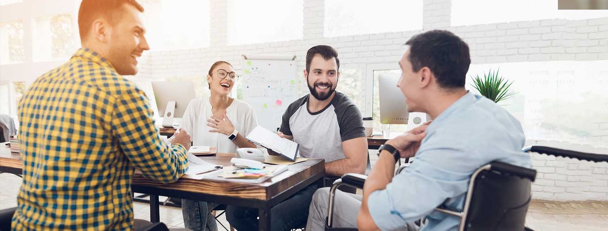 Four men sitting around a table during a casual meeting or discussion in a bright office space.