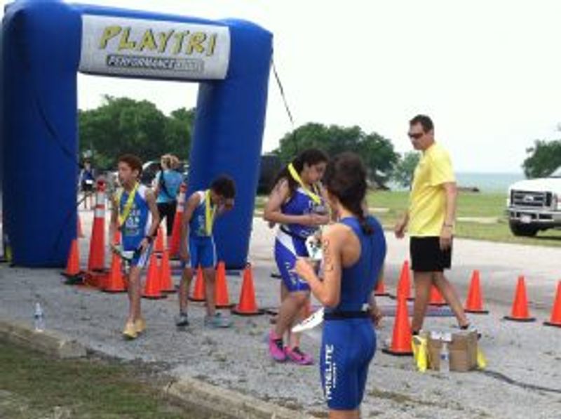 Children running race at outdoor event with blue inflatable start arch and cones.