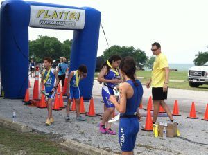 Children running race at outdoor event with blue inflatable start arch and cones.