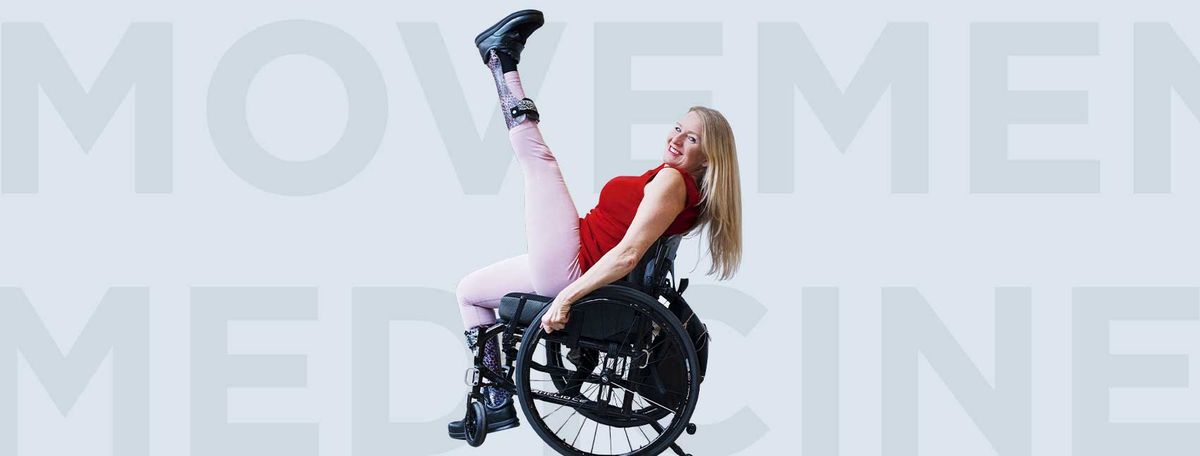 Woman in red shirt performing wheelchair stunt with leg raised, "MOVEMENT" text visible in background.