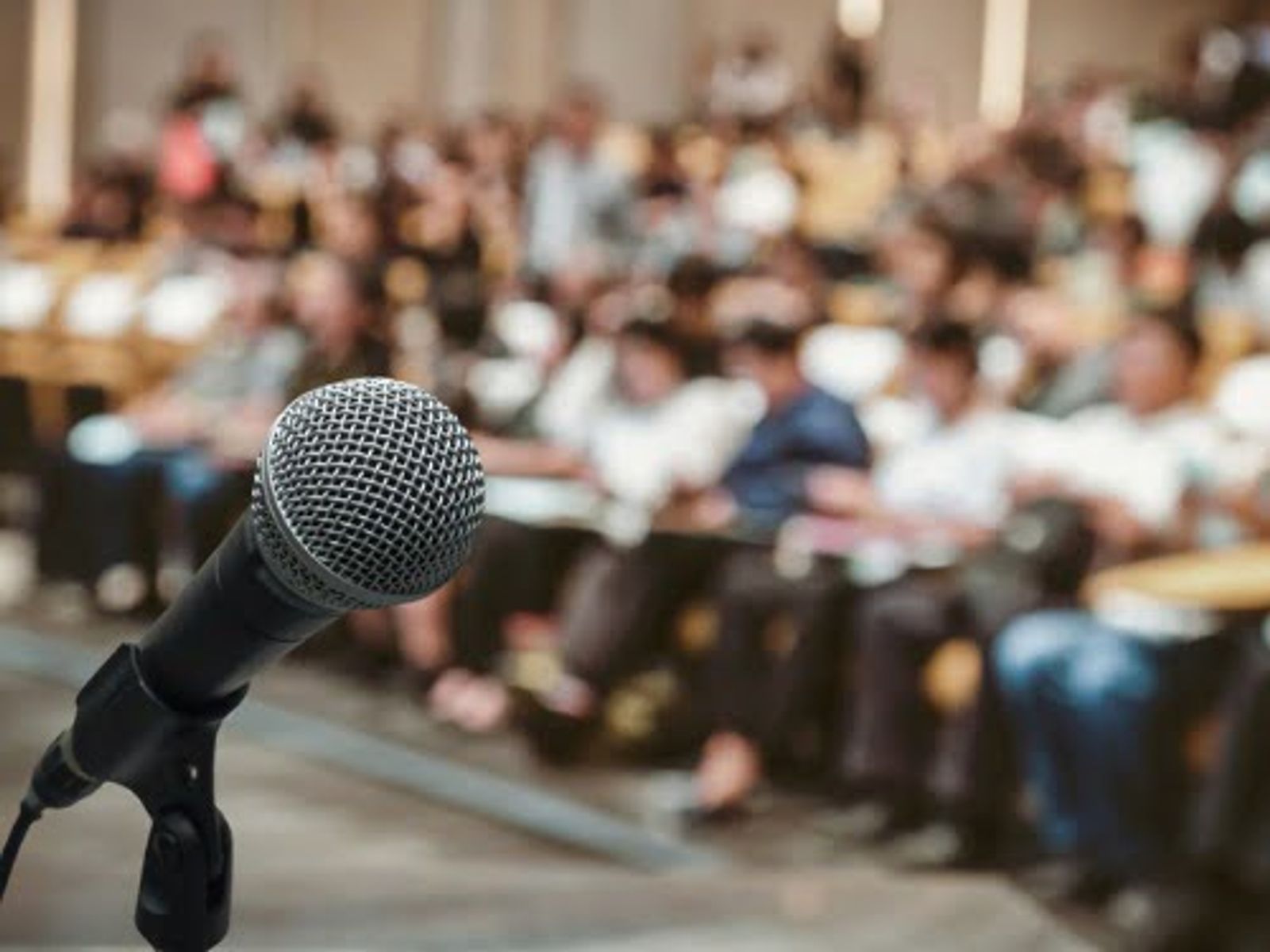 Microphone in foreground with blurred audience seated in background auditorium.