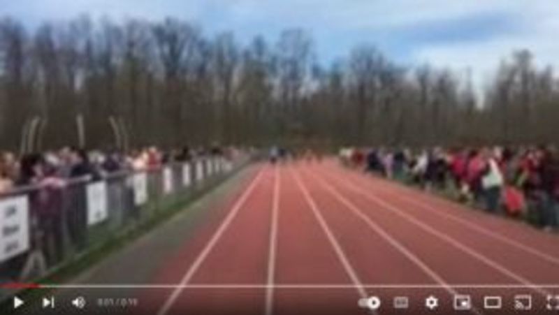 Evento de atletismo con espectadores a ambos lados de la pista roja de carreras.