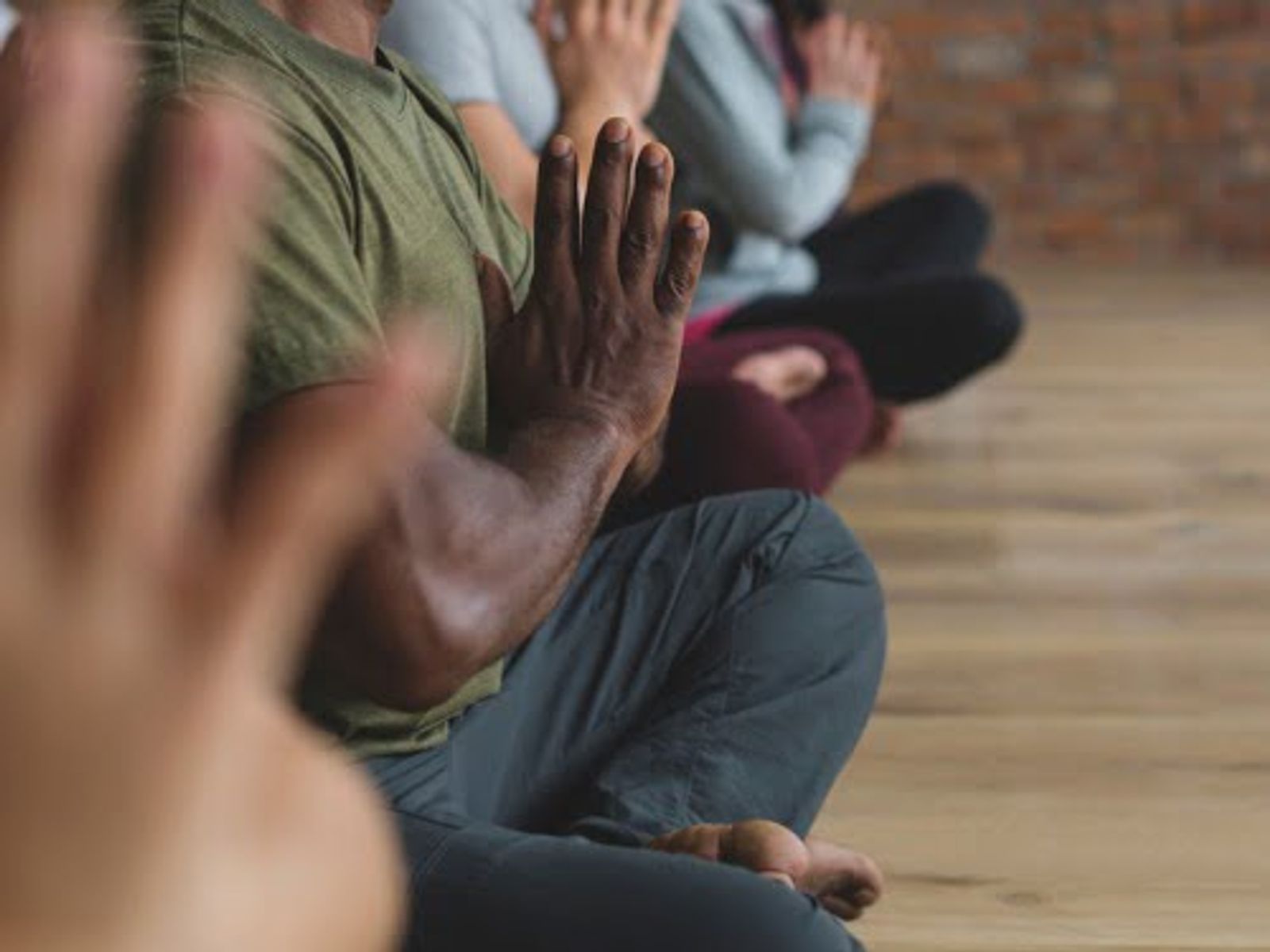 Grupo de personas sentadas en un piso de madera con las manos levantadas en posición de oración o meditación.