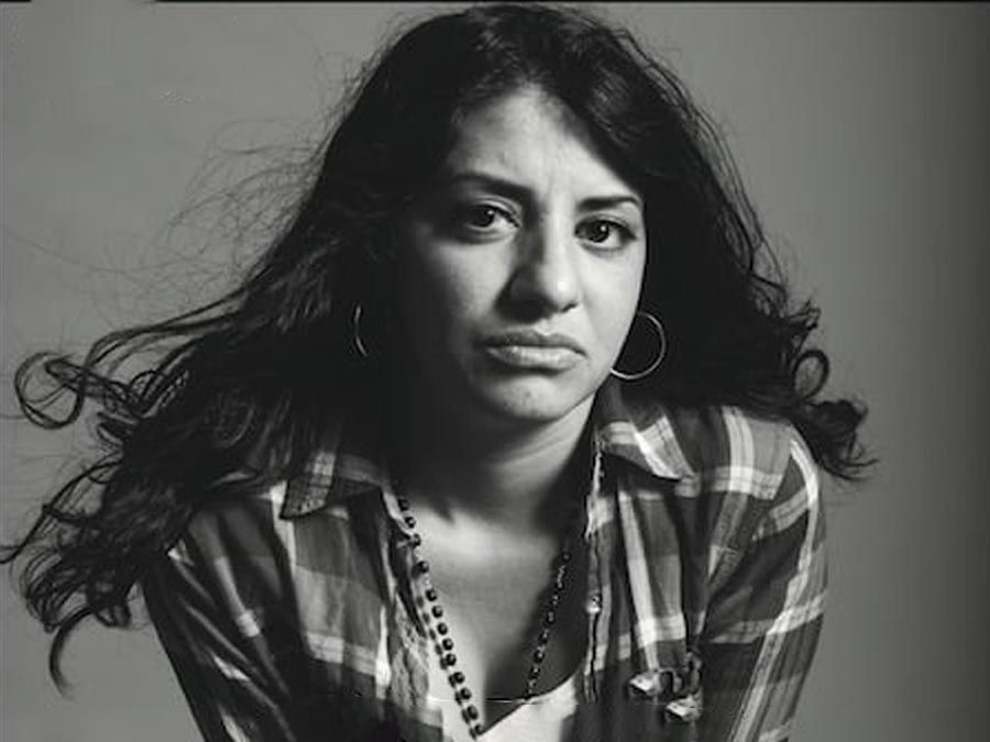 Retrato en blanco y negro de una mujer con cabello largo y oscuro, que lleva una camisa a cuadros y aretes de aro.